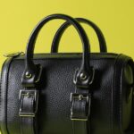 黄色の背景に置かれた黒い革のハンドバッグ